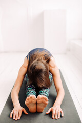 A woman doing yoga on yoga mat in bright minimalistic space. 