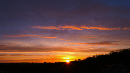 Amazing sunrise in rural scene. Dramatic sky with sunbeam and stratus clouds over the silhouette of hill on the horizon.