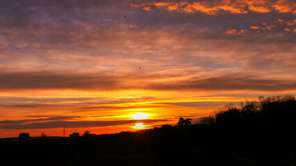 Amazing sunrise in rural scene. Dramatic sky with sunbeam and stratus clouds over the silhouette of hill on the horizon.