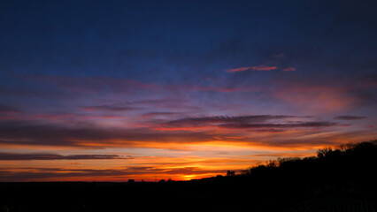 Amazing sunrise in rural scene. Dramatic sky with sunbeam and stratus clouds over the silhouette of hill on the horizon.