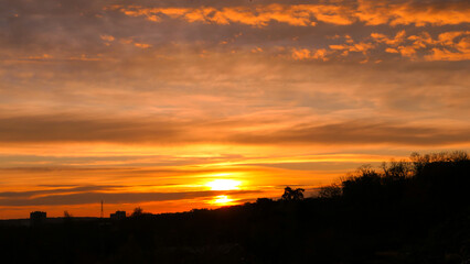 Amazing sunrise in rural scene. Dramatic sky with sunbeam and stratus clouds over the silhouette of hill on the horizon.
