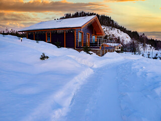 One-storey hotel. Country hotelat background of dawn.  Winter landscape with a wooden house. Snow-covered path leads to cottage village. Winter village landscape.Winter in cottage village.