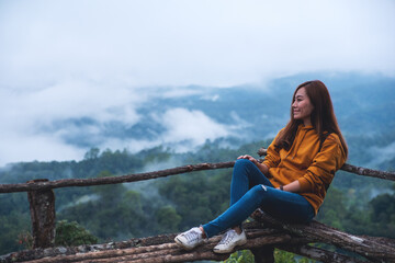 Portrait image of a female traveler sitting and looking at a beautiful mountain and nature view on foggy day