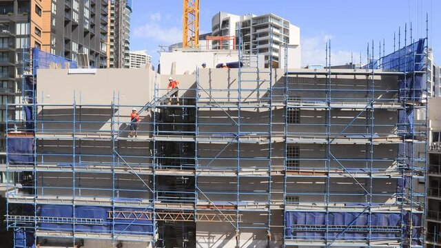 Construction workers on scaffolds building high-rise house as timelapse in 4k.
