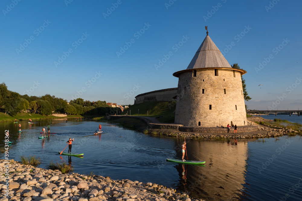 Poster Pskov, Russia: august 21, 2020:  SUP surfers on Pskova river. Towers and wall of Pskov Kremlin at background.