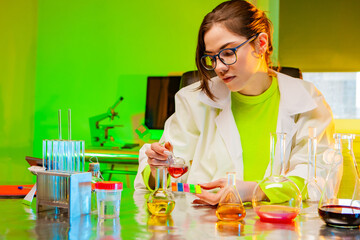 Chemical laboratory in neon color. A laboratory assistant girl is sitting at a table with chemical dishes. The chemist compares the color of the liquid in the test tube with the test strips. Chemistry
