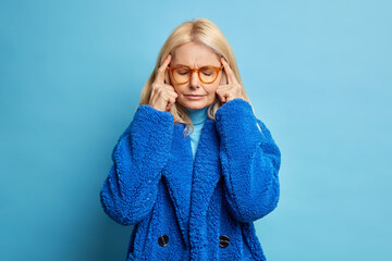 Depressed blonde forty years old woman keeps fingers on temples thinks deeply or has headache...