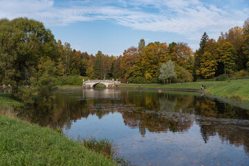Fototapeta na wymiar Vintage Viskontiev bridge over Slavyanka river. The autumn landscape. Pavlovsk Palace Park. Saint-Petersburg, Russia