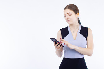 Fototapeta premium Slender young girl with a mobile phone. The girl watches news on the Internet on her smartphone. A woman with a phone on a light background. Place for the label. The girl with the manicure.