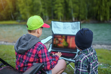 children watching movies on a laptop on the beach of forest river