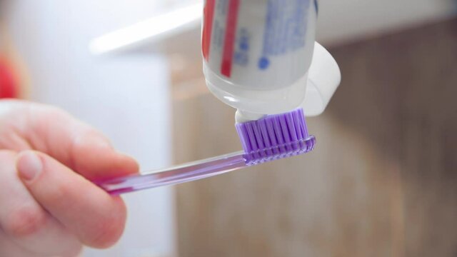 Female hand squeezing tooth paste on blue toothbrush in bathroom
