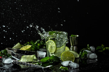 Fototapeta na wymiar Summer homemade lemonade made from lime, lemon, cucumber with ice in glass, drink with liquid splash, freeze motion in jar glass on dark background