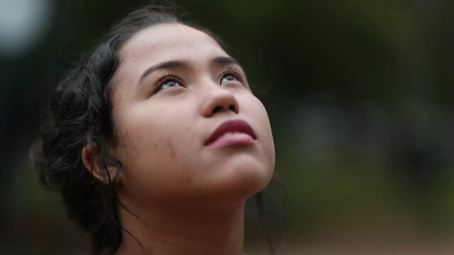 Hispanic young woman face in contemplation loooking up at the sky with hope and faith
