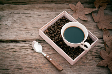 black coffee in white mug with maple leaf on wooden table in vintage style