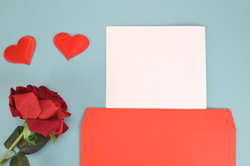A red rose bud and two decorative hearts next to an envelope and a blank page for congratulations on a blue background.