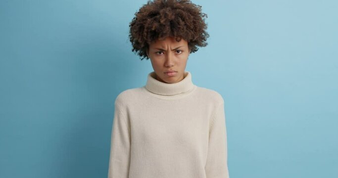 Unhappy serious Afro American woman shakes head says no and disagrees with someone expresses disapproval denies something wears casual white sweater poses against blue background. Denial concept