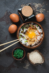 Japanese-style rice and egg bowl or tamago kake gohan, top view on a brown stone background, vertical shot