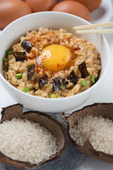 Bowl of japanese warm rice mixed with a raw egg and topped with an egg yolk, vertical shot, close-up