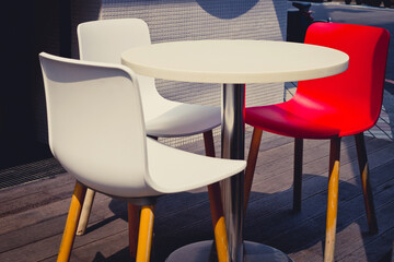 A white table, two white chairs and a red chair putting outside a cafe. 