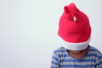 boy hiding underneath a red christmas hat with grey background