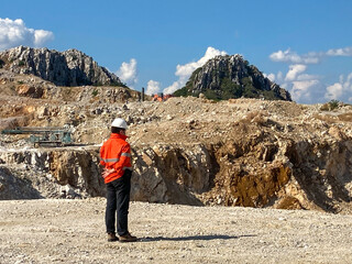 Landscape shot of rock and concrete mine that surround with stone, mountain and blue sky. With Industrial engineer who monitoring worker who driving truck and drilling machine. Industrial concept.