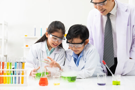 Young Asian boy and girl student wearing protective google while study and do science experiment in classroom with teacher. Learning and having fun moment. Chemist or biology classroom concept.