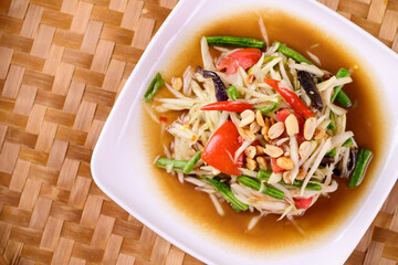 Thai food (Som Tum), Spicy green papaya salad on woven bamboo background, Top view