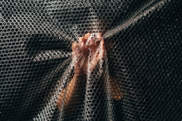 Plastic pollution. Ecology problem. Environmental protection. Textured art portrait of unrecognizable woman hand crumpling bubble wrap wall on black background.