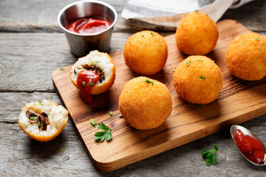 Homemade Fried Risotto Arancini stuffed with mushroom and parmesan cheese, served with tomato sauce. - Powered by Adobe