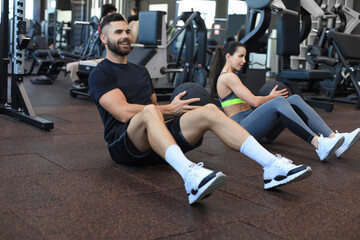 Naklejka na ściany i meble Sport young people sitting on a gym floor working out together with a medicine ball during an abdominal exercise session.