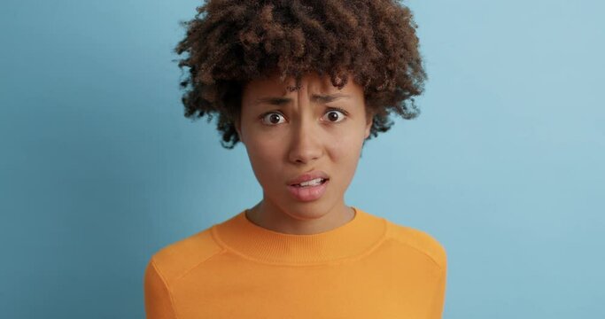 Displeased dark skinned woman looks with aversion and dissatisfaction aside dislikes something says its not good dressed in casual jumper isolated over blue background. Negative emotions concept