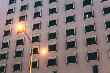 A lit street lamp in front of a tall building at night. Toned image.