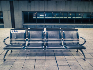 Metal seats on railway station platform. Sign of "Priority seats" on one of the chairs. Toned image. 