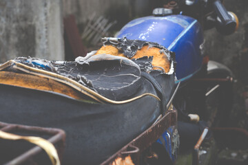 An old, weathered motorbike with ripped cushion. Damaged motorcycle seat. Close up detail of old and torn motorbike seat with visible foam.Toned image. 