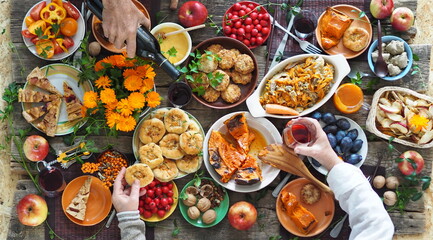 Country style. Thanksgiving table. Lots of food with red wine. The guests eat food with their hands over the set table. View from above.