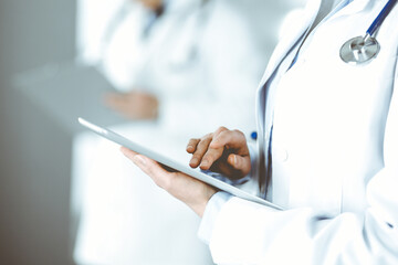 Fototapeta premium Unknown woman doctor is checking some data at computer tablet, close up. Young doctors at work in a hospital. Medicine and healthcare concept