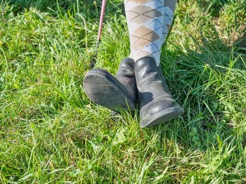 Young girl in paddock boots with long tighs sitting in meadow and waiting for her horse and riding lesson.