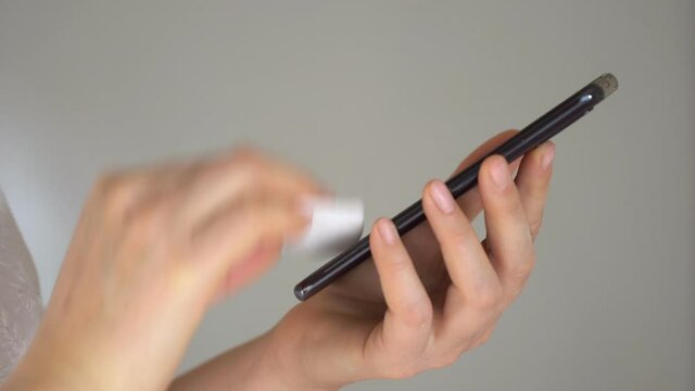 Close-up of woman hand using wet wipe and sanitizer to clean cell phone screen. People cleaning and disinfecting mobile telephone monitor to kill virus and germs. Female hands holding smartphone