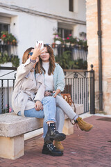 Two young women sitting on a bench and making selfie in the street.