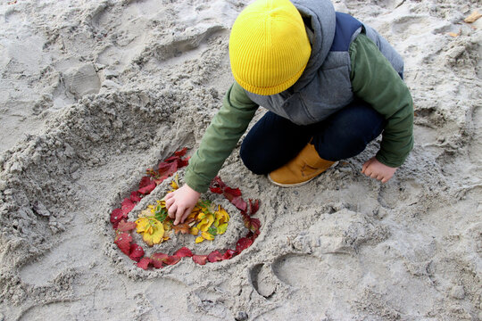 A child draws a heart in the sand. 