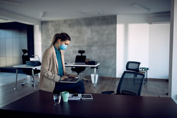 Businesswoman with face mask working on laptop in the office.