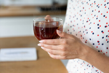 Crop close up of woman hold cup with hot tea enjoy cozy domestic evening at home. Female renter or tenant drink warm beverage relax rest on leisure weekend in own house. Hygge, relaxation concept.
