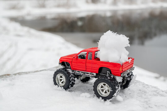 Red toy pickup truck carries fluffy snowball in its back. Winter outdoor fun activities