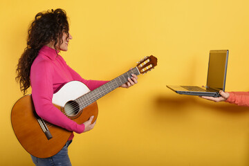 Happy woman follows a guitar lesson online. Yellow background