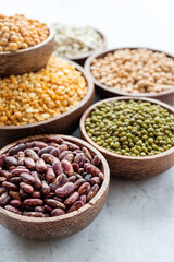 Various dried legumes in wooden bowls on white marble background