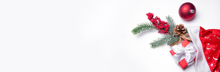 Christmas background on white: one single red Christmas toys, fir branch with a cone and berries and red gift box with white ribbon in the Santa Claus hat, space for text, Christmas banner
