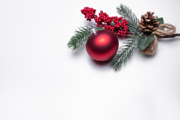 Single red Christmas ball on a white background under a spruce branch with red berries and a cone on a white background: Christmas background with space for text