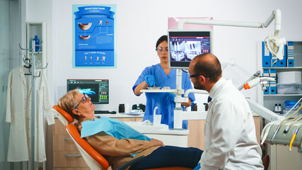 Man dentistry doctor pointing on digital screen showing dental implants. Dentist and nurse working together in modern stomatological clinic, explaining radiography of teeth on monitor