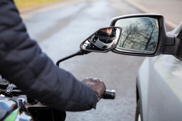 Motorcyclist does not keep distance while riding side by side with a car, side mirrors touching