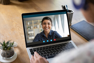 Close up of woman look at laptop screen talk on video call with ethnic colleague coworker. Rear view of employee have webcam conference or online meeting with international client from home office.